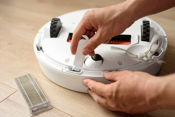 a man cleans the sensor on a robot vacuum cleaner with a special brush - obrazy, fototapety, plakaty