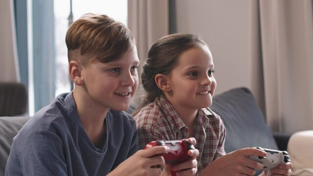 Medium close up of excited brother and sister age 12 and 10 sitting on sofa and playing video games together