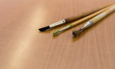 Fototapeta premium Three artistic brushes lie on the table close-up. The objects for drawing with paints are put together. Wooden tassels made of squirrel and horse hair.