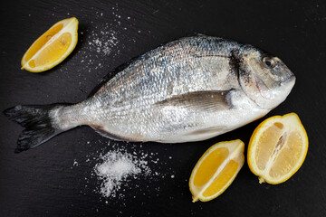 Fototapeta na wymiar fresh fish wth lemon and salt on black ceramic