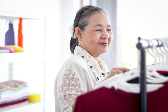 Happy Smiling Senior Elderly Woman Housewife Hanging Clothes Indoor To Dry, Older Asian Female Doing Laundry At Laundry Room, Dried Laundry, Grandma Doing Housework And Cleaning Clothes At House