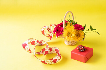 贈り物とハートのリボンとヒマワリのような細い花びらの黄色のガーベラ（イエロースパイダー）と赤のガーベラの花かご