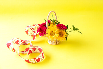 ハートのリボンとヒマワリのような細い花びらの黄色のガーベラ（イエロースパイダー）と赤のガーベラの花かご