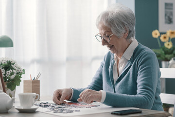 Happy elderly woman solving a puzzle and drinking tea