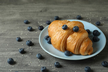 Plate with croissant and blueberry on gray textured table
