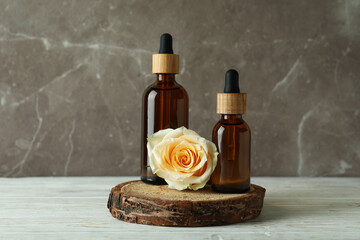 Bottles with rose essential oil and rose on white wooden table