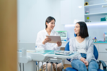Fototapeta premium Asian female dentist showing x-ray on tablet, giving treatment advice.