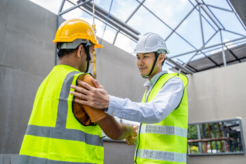 Asian male engineer and worker making handshake on construction site.