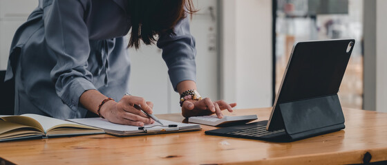 businesswoman or accountant taking note and working on calculator and laptop computer to calculate...