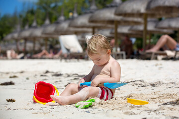 Cute baby boy playing with beach toys on tropical beach