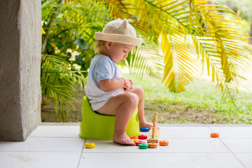 Sweet toddler boy, sitting on potty on a back porch in a holiday resort patio