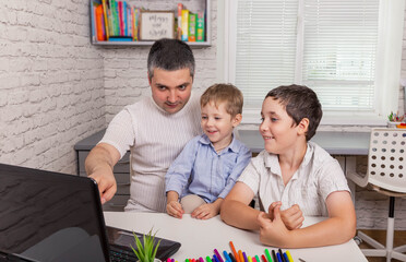 Family with kids shopping or watching video online. Young parent and boys are using a laptop at home. Dad with sons using laptop together looking at screen. Online remote learning. Video conference