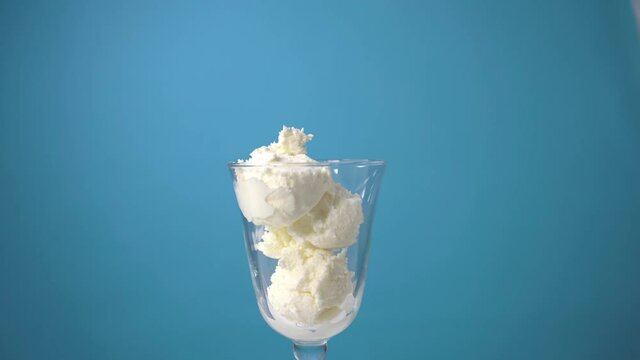 Place vanilla ice cream in a glass. Make balls of white ice cream with a special spoon. Cooking delicious ice cream on a blue background. Summer dessert in a cafe.