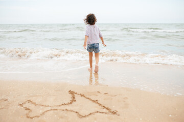 Fototapeta na wymiar Five years cute curlyFive years cute curly caucasian girl painting on sand on the beach. 