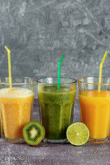 Three glasses in a row with orange juice and banana orange kiwi smoothie