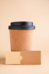 Business card mockup, eco kraft paper on a beige background. A cup for coffee to go made from recycled raw materials. Eco friendly stationery concept. High quality photo. Copy space