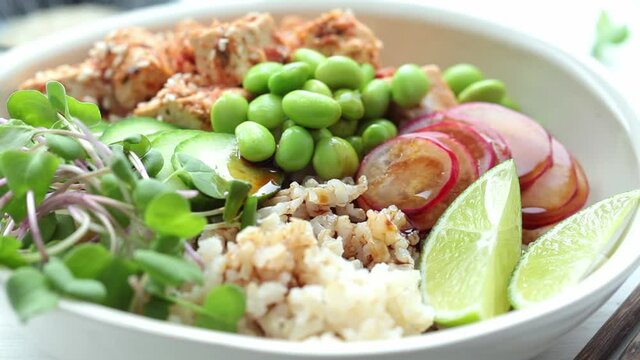 Vegan poke bowl with tofu, brown rice, beans and vegetables pouring soy sauce. Plant-based diet concept.