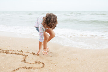 Five years cute curlyFive years cute curly caucasian girl painting on sand on the beach. 