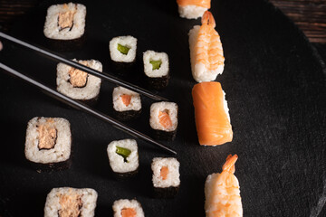 Unterschiedliche Sushi sind aufgelegt auf der schwarzen Platte, Schwarze Stäbe fassen ein Sushi an. Sehr gut geeignet für chinesischen Restaurant, Querformat