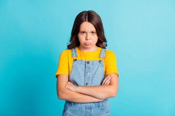 Photo of funny upset small school girl wear denim jeans overall arms folded isolated blue color...