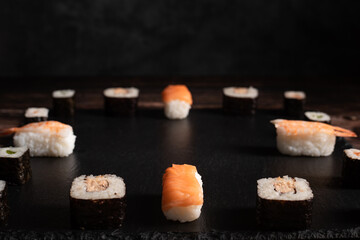 Sushi liegt auf dem schwarzen Brett. Aufgelegt wie eine Uhr. Hintergrund ist dunkel. Querformat. Chinesische Küche, Asia Essen. Passt sehr gut für die  chinesischen Restaurants. Hintergrund