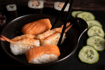 Garnellen und  Sushi liegen in der schwarzen Pfanne, Schwarze japanische Stäbchen halten sushi fest, Die Pfanne steht auf dem schwarzen hintergrund, Asiatisches Essen, gesund und lecker, Restaurant