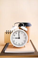 White alarm clock with arrows at nine in the morning and stationery made from recyclable material, coffee cup. Vintage watch on a beige background. Copy space. High quality photo