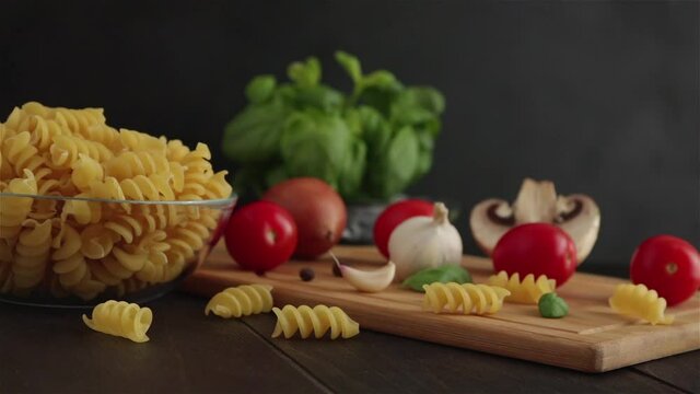 pasta ingreidents panning shot.fusilli cherry tomatoes basil garlic mushroom on black wooden background