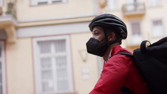Young courier delivering a food on bike, looking for adress. Coronavirus concept.