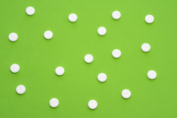 White tablets scattered on green background form a speckled ornament. Photo for use in medicine, pharmacy, pharmaceutical production and marketing, treatment of diseases of the gastrointestinal tract