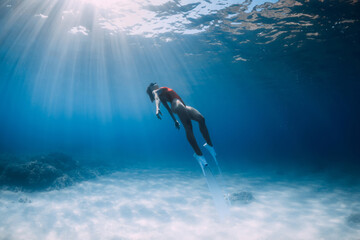 Attractive free diver with white fins glides and posing underwater in blue ocean with sunlight....
