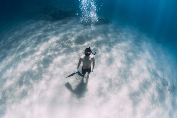 Obraz na płótnie Canvas Sporty freediver stay on sandy bottom with fins underwater in sea.