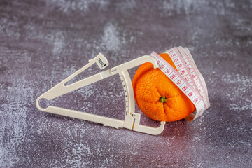 Orange wrapped with measuring tape and caliper on a gray concrete background.