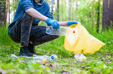 Garbage collection in nature. Young man collects plastic trash in summer forest