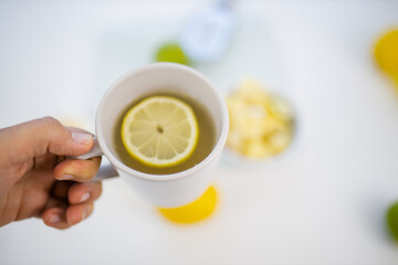 Female hand holding a cup of lemon tea above limes and lemons