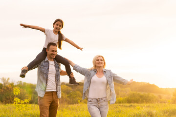 Fototapeta premium Happy family in the park evening light. The lights of a sun. Mom, dad and baby happy walk at sunset. The concept of a happy family