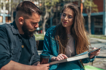 Two students sitting on a bench in a campus and studying for their exam