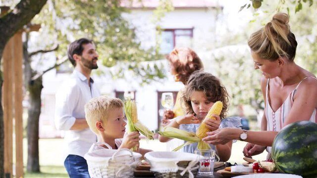 Family having a garden party, kids peeling corn.