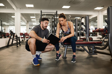 Male personal trainer showing female client workout progress clipboard - obrazy, fototapety, plakaty