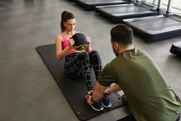 Male personal trainer assisting woman in weighted ball sit up crunches