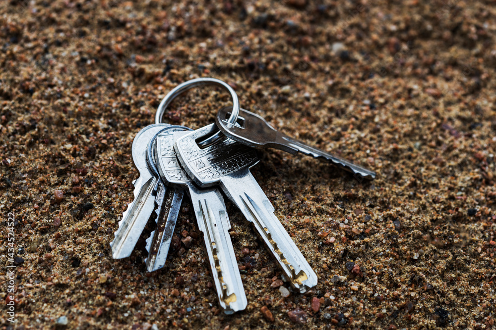 Poster a bunch of silver keys lie on the sand. lost keys