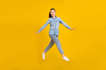 Full length photo of cute excited young woman wear denim shirt smiling jumping high isolated yellow color background