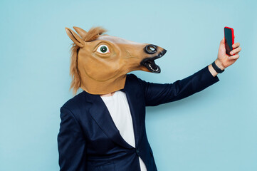 Crazy senior man wearing horse mask and taking selfie with mobile smartphone.
