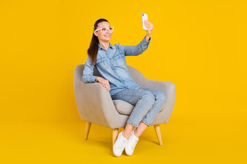 Full size photo of charming happy attractive woman sit chair make selfie isolated on shine yellow color background