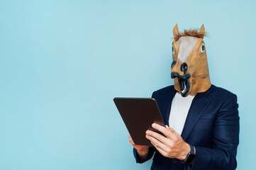 Young man in funny horse mask works with a portable tablet.