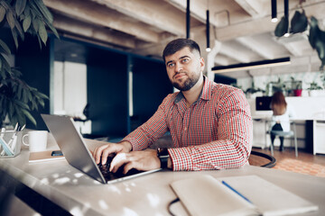 Obraz premium Young man in casual shirt working on computer in office