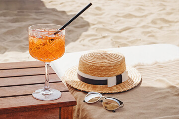 A glass of aperol Spritz , straw hat and sunglasses on the beach