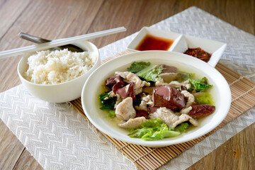 Boiled soup blood pork in bowl and flavouring in white bowl on bamboo mat,