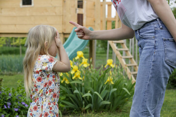 Mother is shouting at her daughter in public park. Upset little girl is crying in front of her...