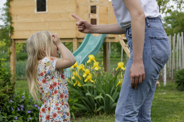 Mother is shouting at her daughter in public park. Upset little girl is crying in front of her...